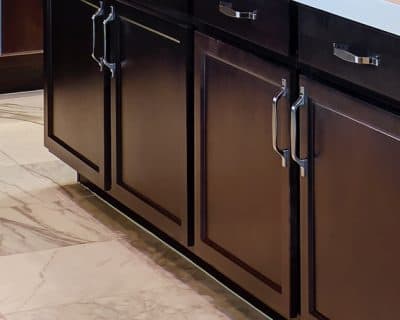 Closeup of dark lower cabinets and drawers with stainless steel handles and marble floor.