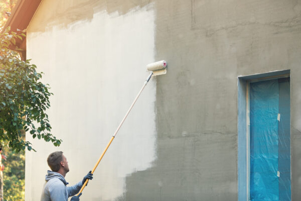 House painter painting building exterior with roller.